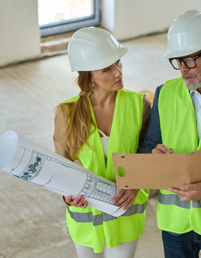 Foreman man holds an open folder and discusses with the real estate manager. They stand in an unfinished building